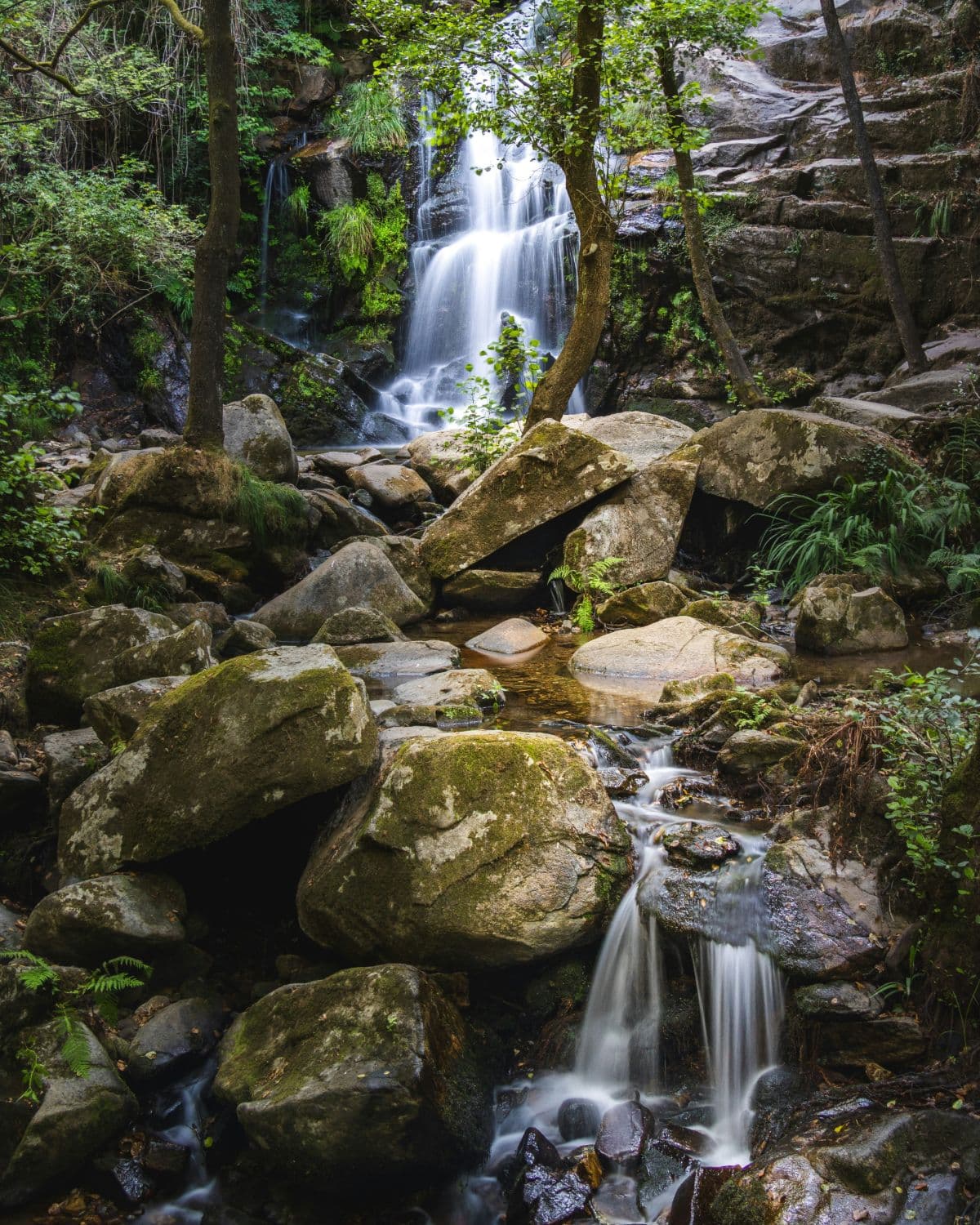 The Cabreia waterfall dropping through woodland into a boulder-strewn stream